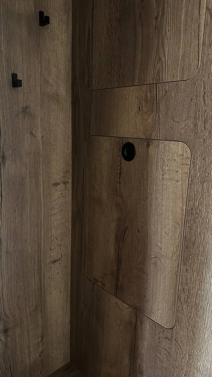 Detail: panel v tmavom dreve s dvierkami so zaoblenými rohmi, okrúhlou úchytkou a čiernymi háčikmi