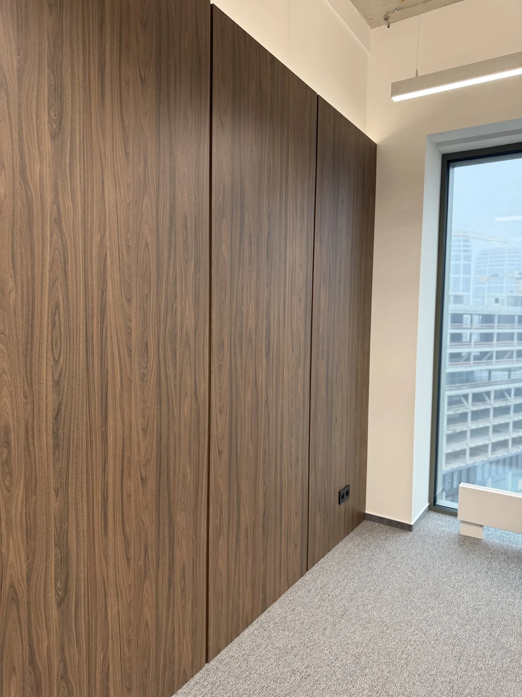 Mit dunklem Holz verkleidete Wand bis zur Decke, daneben ein Fenster zur Stadt