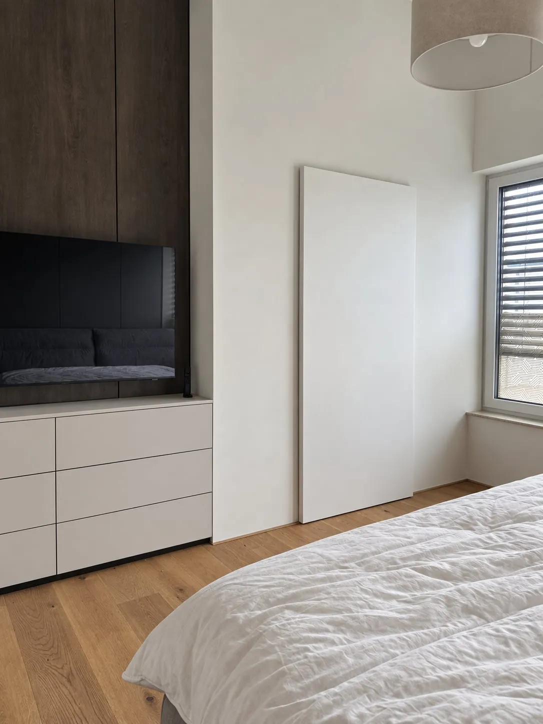 Tmavé panely za televízorom a biela komoda so zásuvkami bez úchytiek