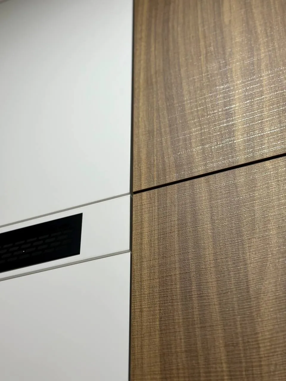 Detail: biely front s čiernou vetracou mriežkou vedľa dvierok v dreve