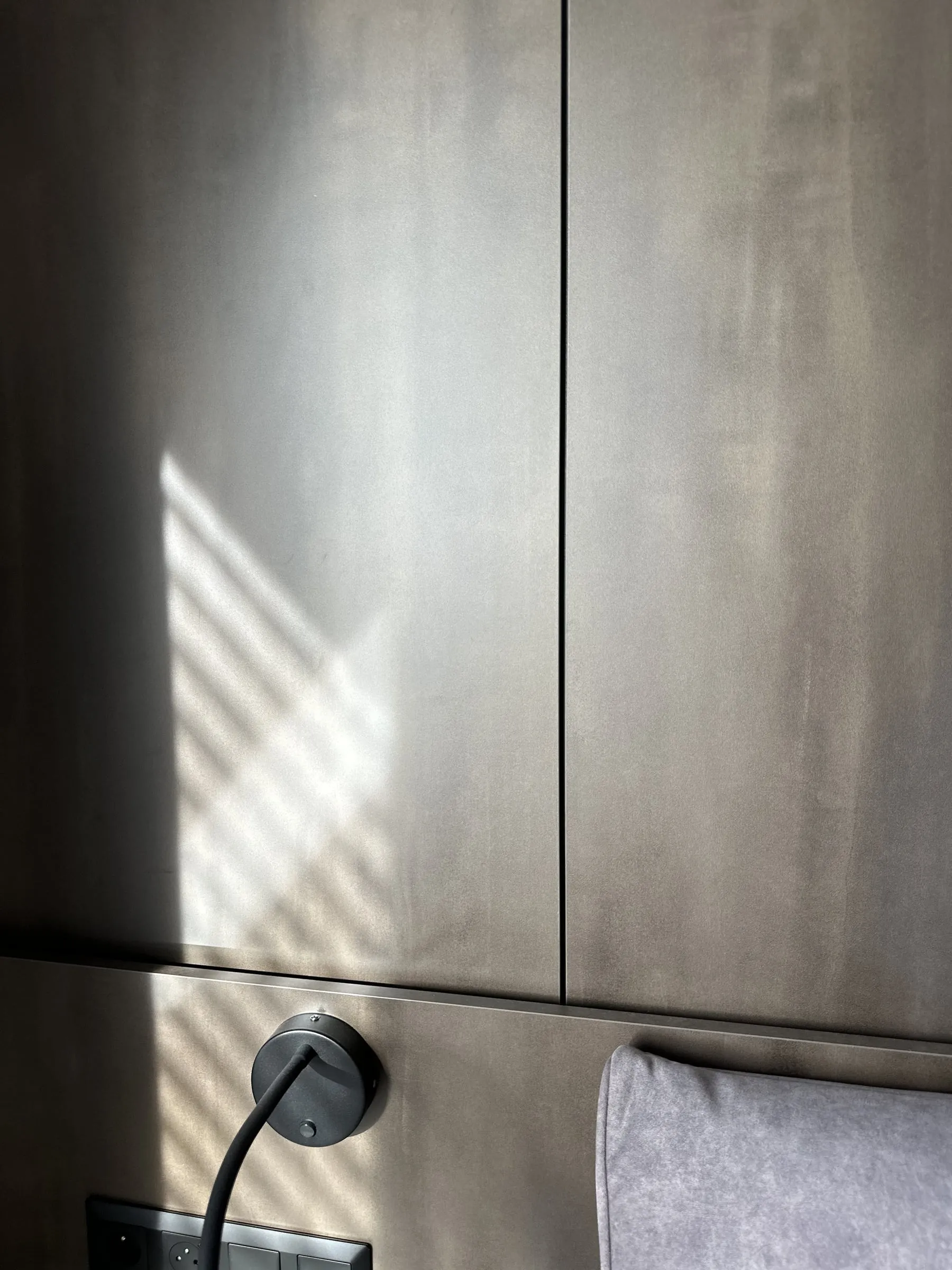 Detail: škára medzi tmavými panelmi a lampička pri čele postele